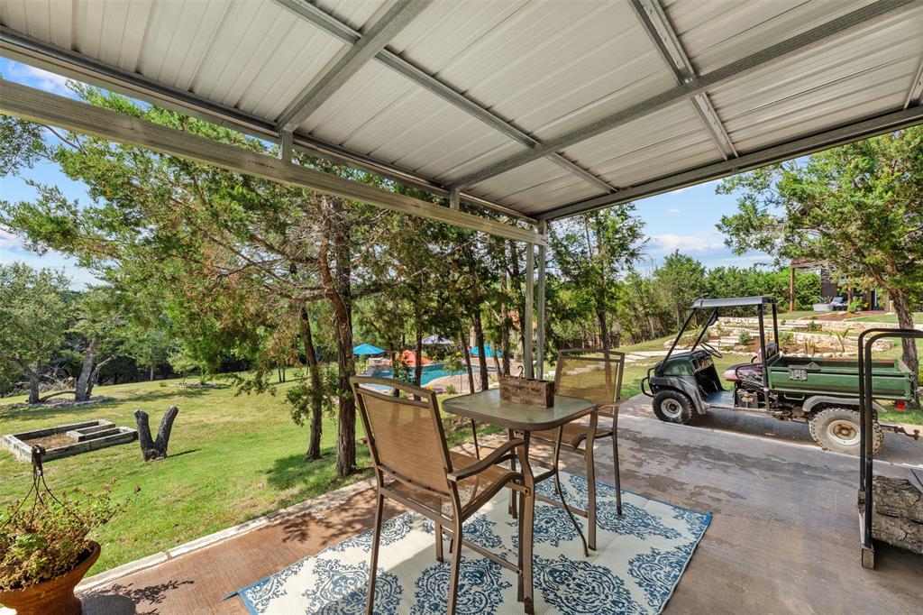 124 Bluffview Circle China Spring, TX 76633 - Photo 36 of 40 Covered patio off shop with metal roofing and structural beams, overlooking a verdant landscape with mature trees and a distant pool area