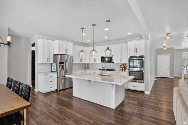 Kitchen featuring an expansive island with a sink, white cabinetry, stainless steel appliances, and pendant lighting