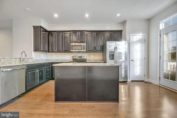 a kitchen with kitchen island granite countertop wooden floors white cabinets and stainless steel appliances