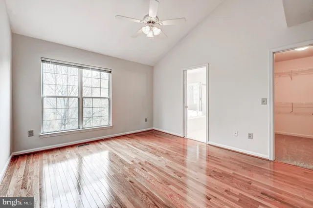 an empty room with wooden floor ceiling fan and windows