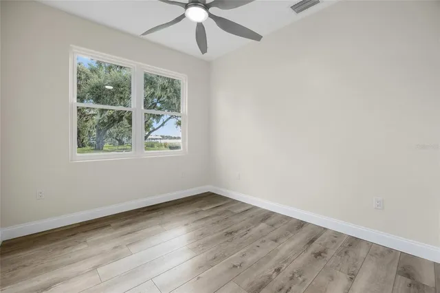 an empty room with wooden floor chandelier fan and windows