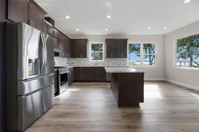 a kitchen with stainless steel appliances granite countertop a refrigerator a sink dishwasher a stove with wooden cabinets and wooden floor