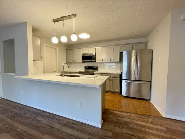 a kitchen with stainless steel appliances a refrigerator a stove top oven a sink dishwasher and white cabinets with wooden floor