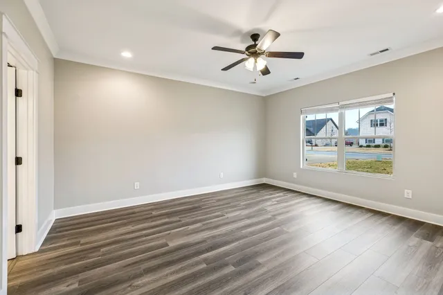 an empty room with wooden floor fan and windows