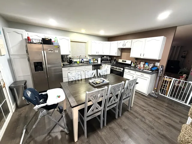 a kitchen with stainless steel appliances granite countertop a refrigerator a microwave a stove and a dining table with wooden floor