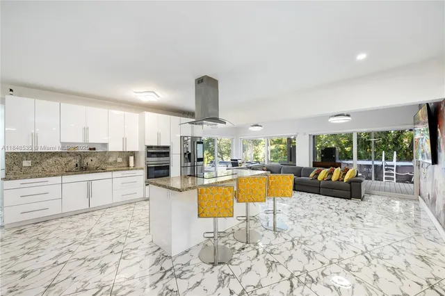 a large kitchen with stainless steel appliances kitchen island granite countertop a refrigerator a stove top oven a dining table and chairs with the wooden floor