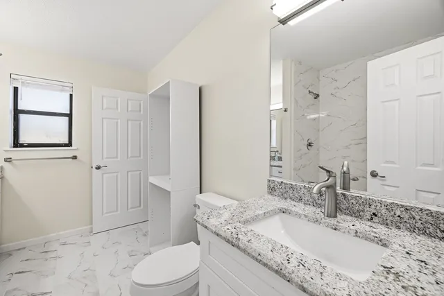 a bathroom with a granite countertop sink toilet a mirror and shower