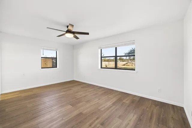 an empty room with wooden floor ceiling fan and windows