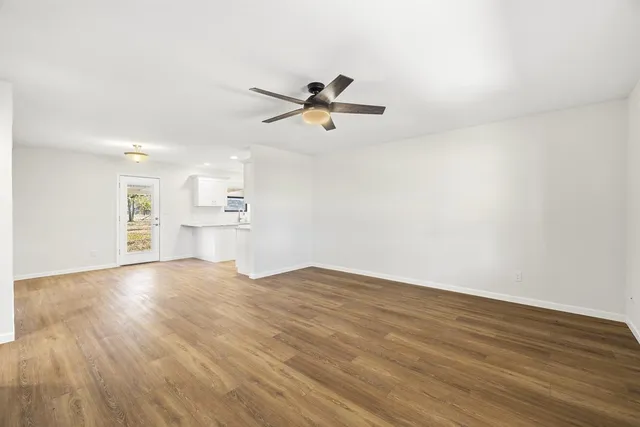 an empty room with wooden floor ceiling fan and windows