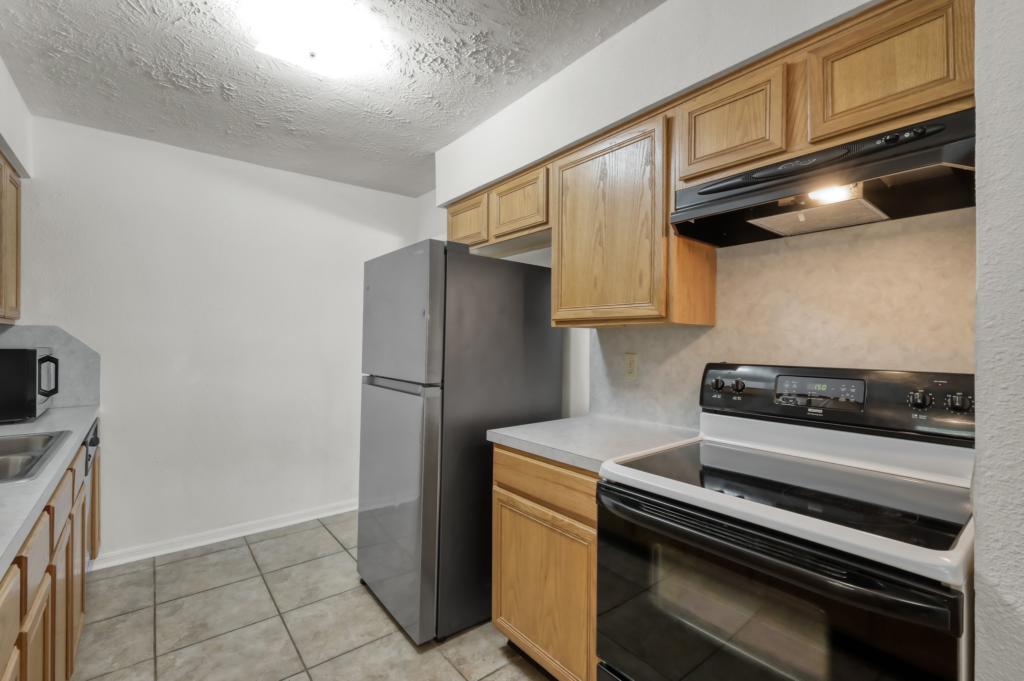 4314 Enchantedgate Drive Spring, TX 77373 - Photo 13 of 47 Kitchen features a clean layout with tiled flooring, wooden cabinets, and modern appliances, including a stainless steel refrigerator and a black electric stove. The kitchen is well-lit, offering a functional area for cooking.