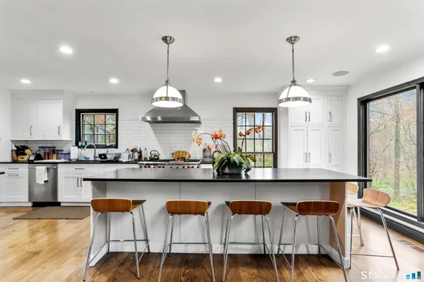 a kitchen with stainless steel appliances granite countertop a sink a stove top oven a dining table and chairs with wooden floor