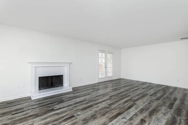 a view of an empty room with wooden floor fireplace and a window