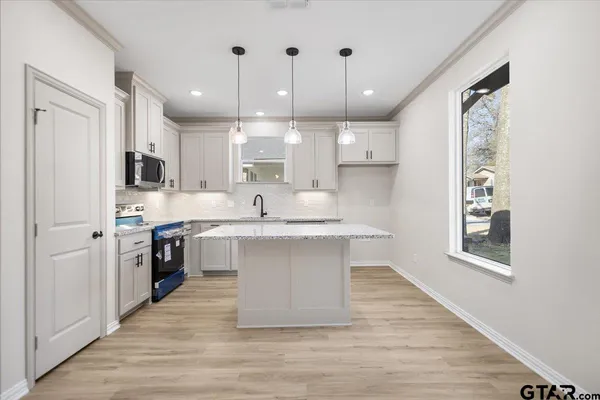 a large white kitchen with kitchen island a sink a center island stainless steel appliances and a window