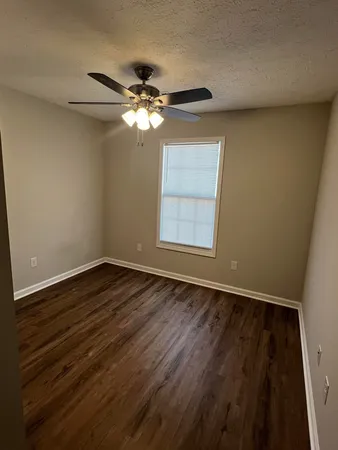 an empty room with wooden floor fan and windows
