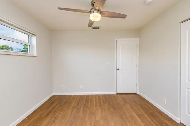 an empty room with wooden floor chandelier fan and windows