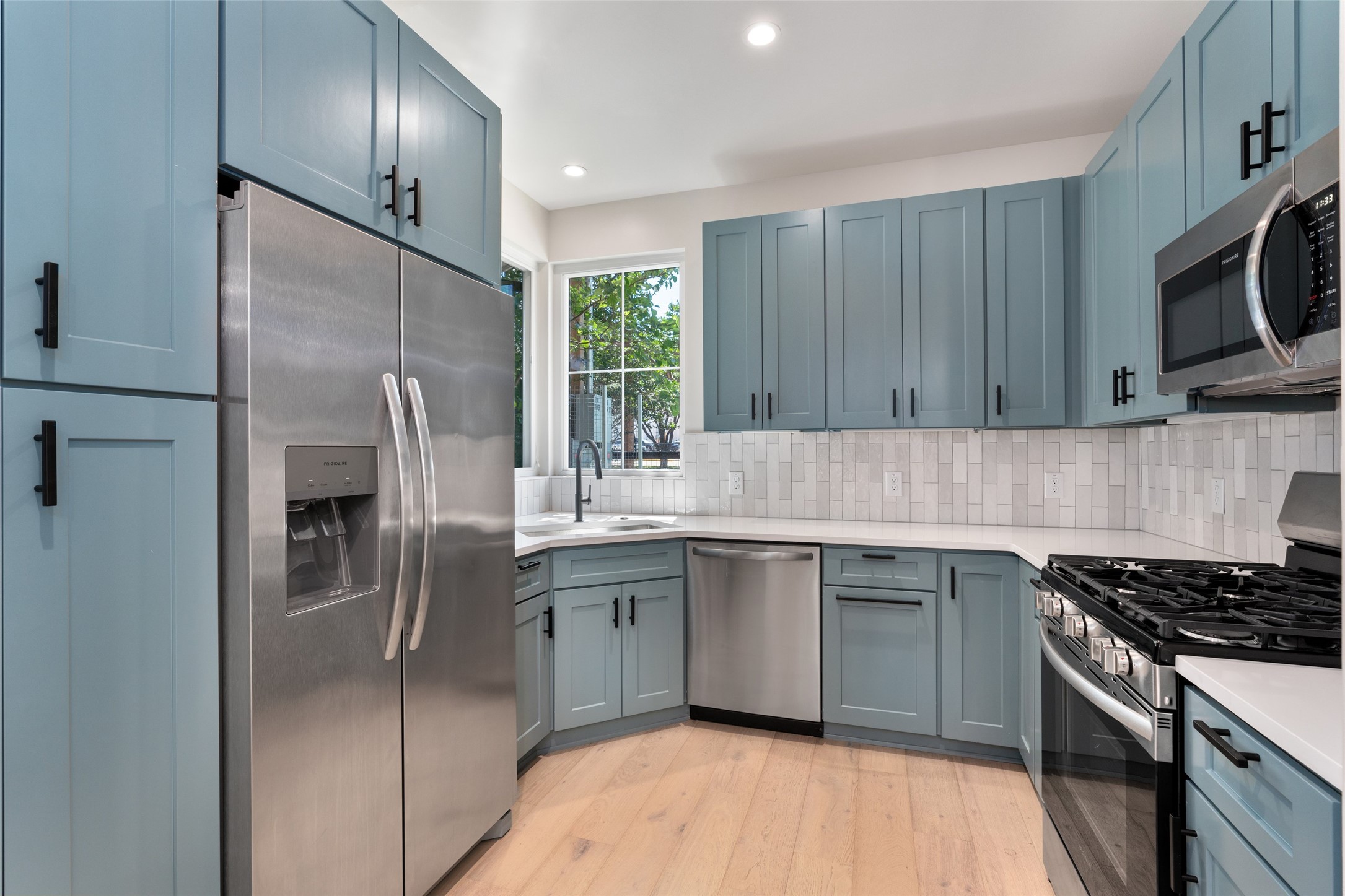 5200 Grover Avenue Austin, TX 78756 - Photo 7 of 32 Kitchen featuring shaker-style cabinetry with matte black hardware, stainless steel appliances, light wood-finish flooring, white countertops, and a subway tile backsplash