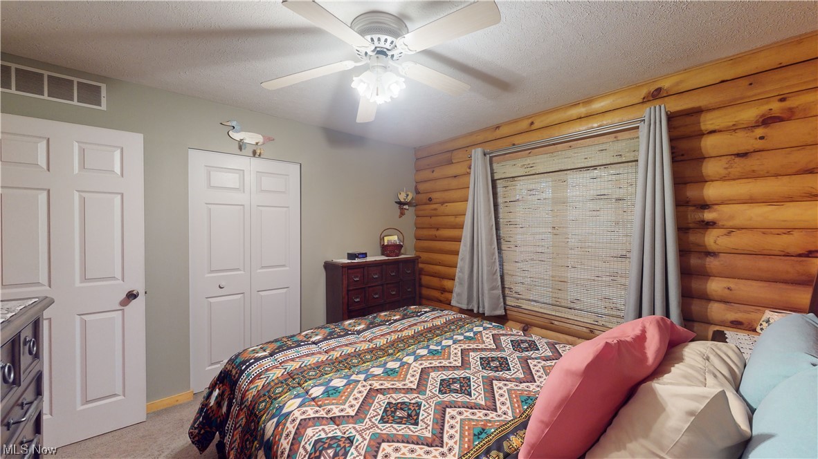 4308 Lyntz Road Warren, OH 44481 - Photo 24 of 34 Bedroom with a textured ceiling, log walls, a closet, light colored carpet, and ceiling fan