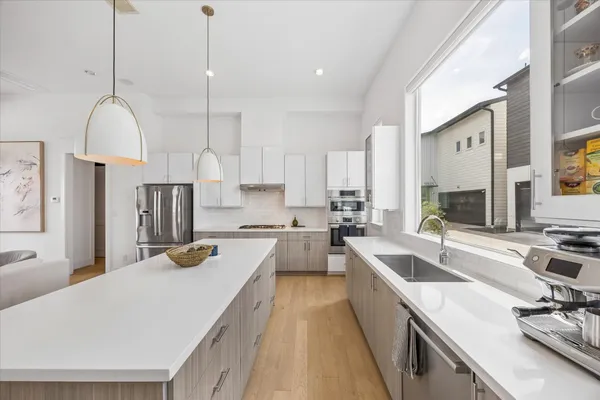 a view of a kitchen with kitchen island a large counter top space a sink stainless steel appliances and cabinets