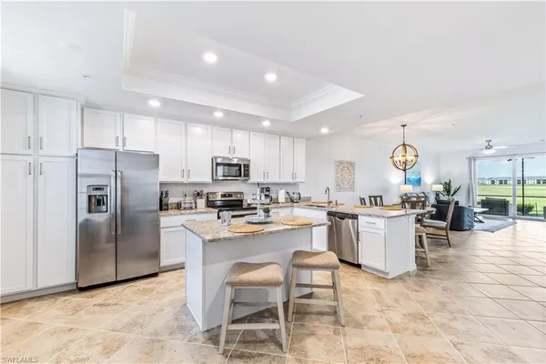 a kitchen with stainless steel appliances granite countertop a refrigerator a stove top oven a sink a dining table and chairs with white cabinets