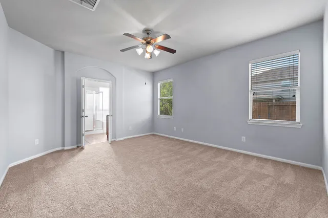 an empty room with a chandelier fan and windows