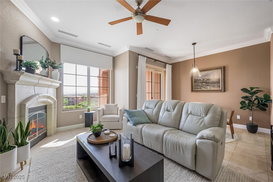 Living area with ornamental molding, light tile patterned floors, a ceiling fan, and a glass covered fireplace