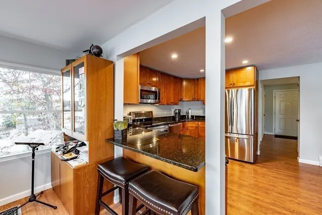 a kitchen with stainless steel appliances granite countertop a refrigerator a stove top oven and a dining table with wooden floor