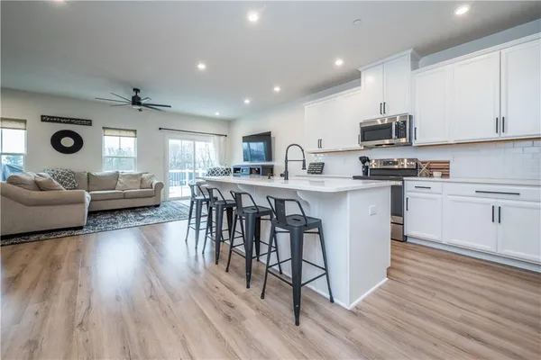a open kitchen with stainless steel appliances granite countertop a stove top oven a sink dishwasher and white cabinets with wooden floor