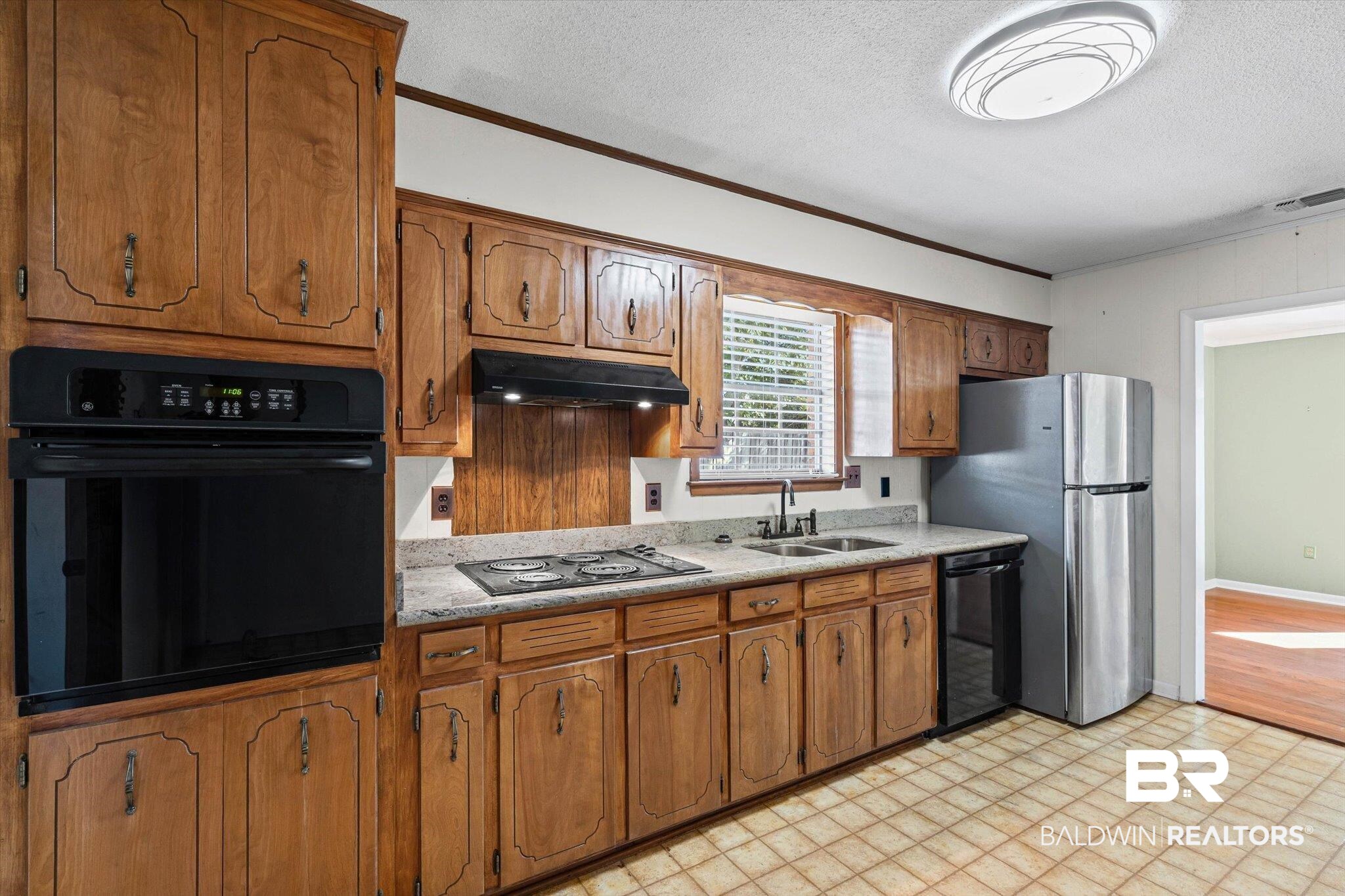 6300 Christopher Drive North Mobile, AL 36609 - Photo 7 of 22 Kitchen with crown molding, a textured ceiling, black appliances, brown cabinetry, and under cabinet range hood