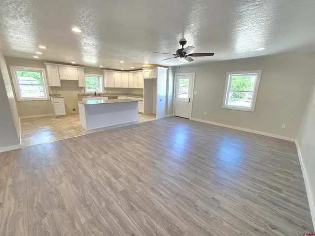 an empty room with wooden floor kitchen view and windows