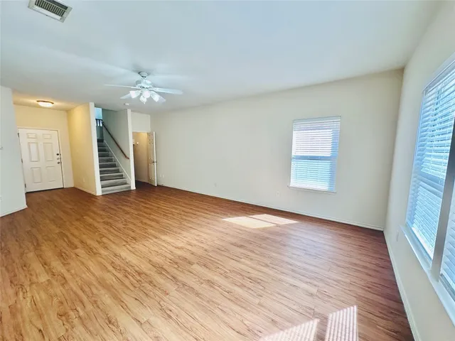 an empty room with wooden floor chandelier fan and windows