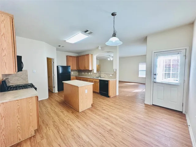 a large kitchen with stainless steel appliances granite countertop a refrigerator a stove a sink dishwasher a oven and a dining table with wooden floor