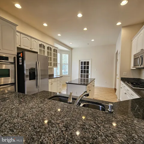 a living room with stainless steel appliances kitchen island granite countertop a refrigerator a stove and a sink with wooden floor