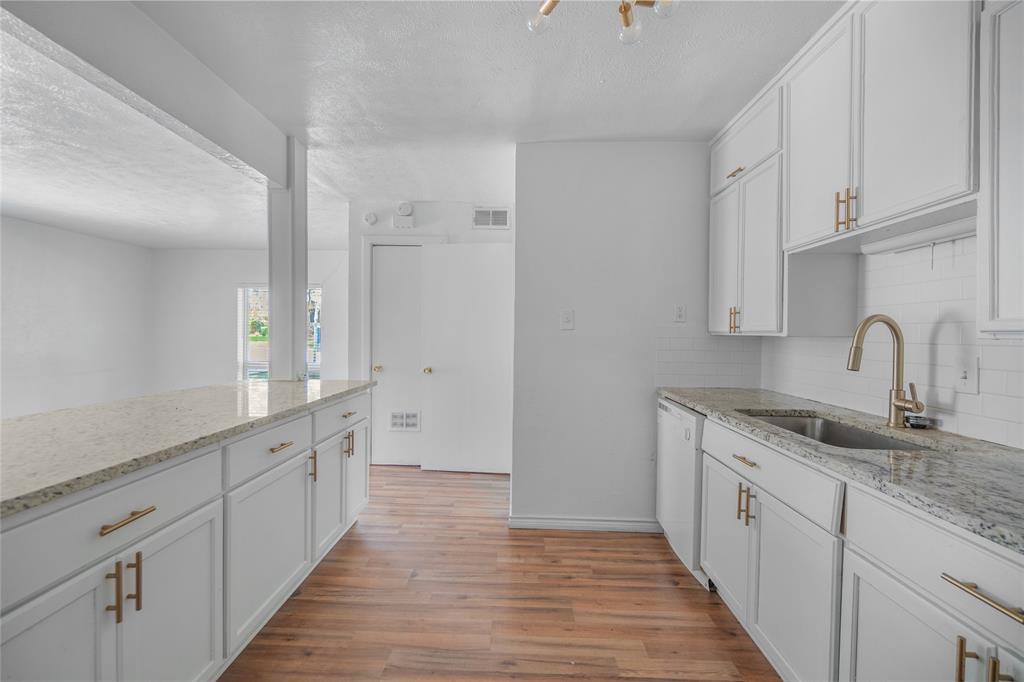 4723 Victor Street, Unit B Dallas, TX 75246 - Photo 5 of 12 Kitchen featuring white shaker cabinetry with gold-tone hardware, granite countertops, a stainless steel sink with a gooseneck faucet, a white subway tile backsplash, and wood-finish flooring