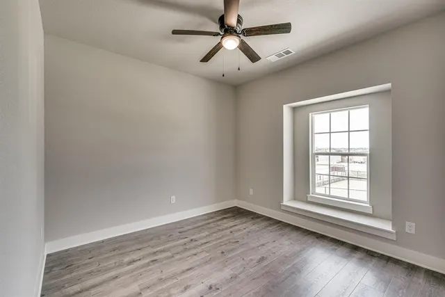 an empty room with wooden floor ceiling fan and windows