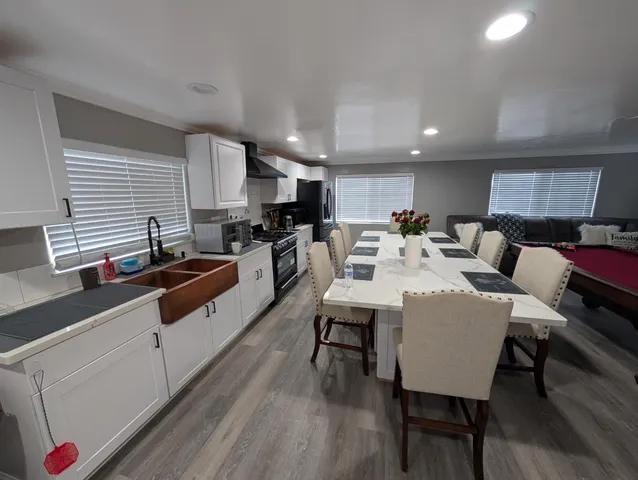 a kitchen with stainless steel appliances kitchen island granite countertop a stove a sink a refrigerator and white cabinets with wooden floor