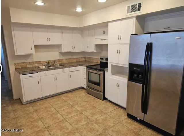 a kitchen with granite countertop a refrigerator stove and white cabinets