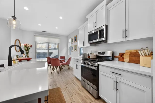 a kitchen with stainless steel appliances granite countertop a stove top oven a sink a dining table and chairs with wooden floor