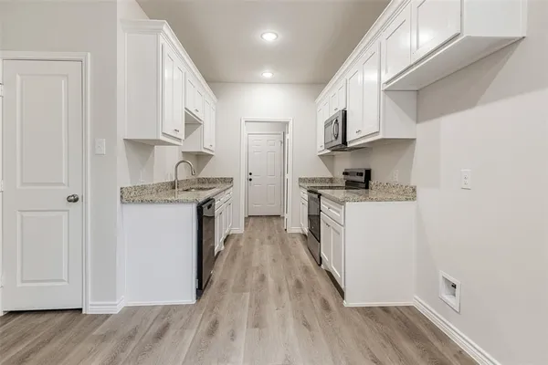 a kitchen with stainless steel appliances granite countertop a refrigerator a stove and white cabinets with wooden floor