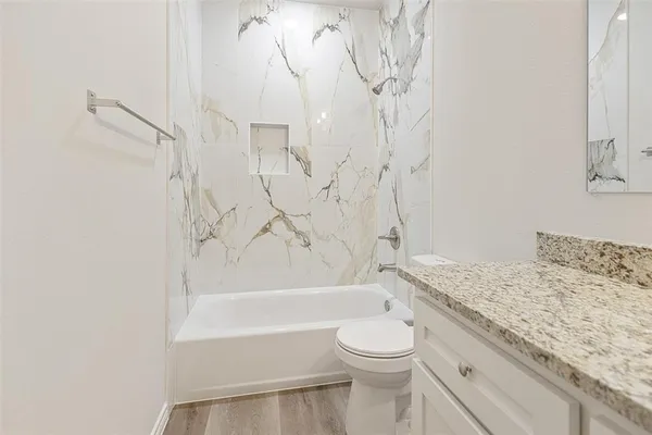 a bathroom with a granite countertop bathtub sink vanity mirror and toilet