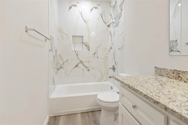 a bathroom with a granite countertop bathtub sink vanity mirror and toilet