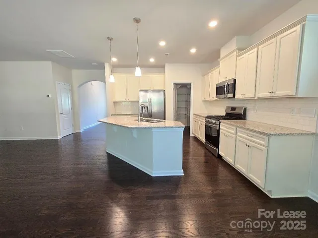 a large kitchen with stainless steel appliances granite countertop a stove a sink a refrigerator and white cabinets with wooden floor