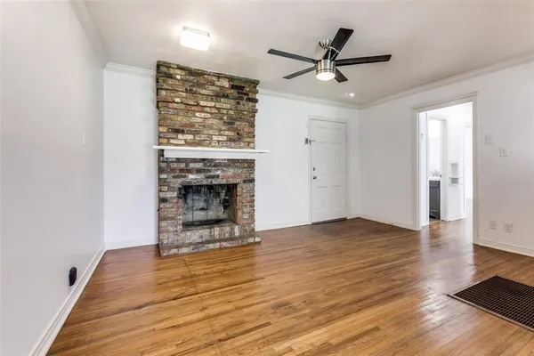 an empty room with wooden floor a ceiling fan a fireplace and windows
