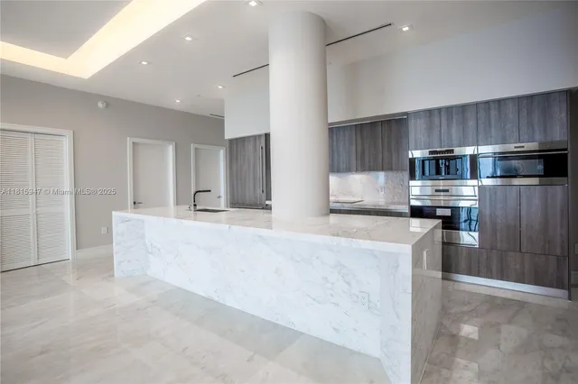 a large kitchen with kitchen island a large counter top stainless steel appliances and cabinets