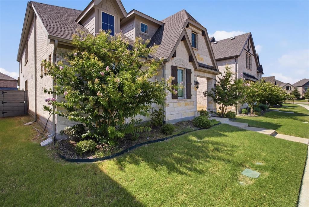 7416 Sequoia Rdg Road Little Elm, TX 76227 - Photo 2 of 37 Exterior facade featuring light-toned stone and brickwork, dark shingle roofing, decorative window shutters, and a well-maintained lawn with mature landscaping