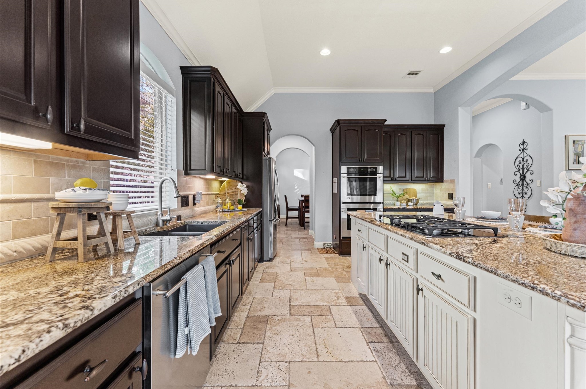 70 Valera Ridge Drive Spring, TX 77389 - Photo 16 of 37 This kitchen features elegant dark wood cabinetry, granite countertops, and a spacious island with a cooktop. It has ample natural light, modern appliances, and a stylish tile floor, creating a warm and inviting space for cooking and entertaining.