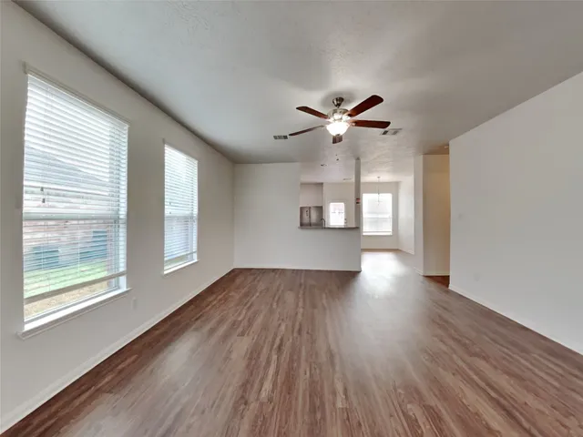 an empty room with wooden floor chandelier fan and windows