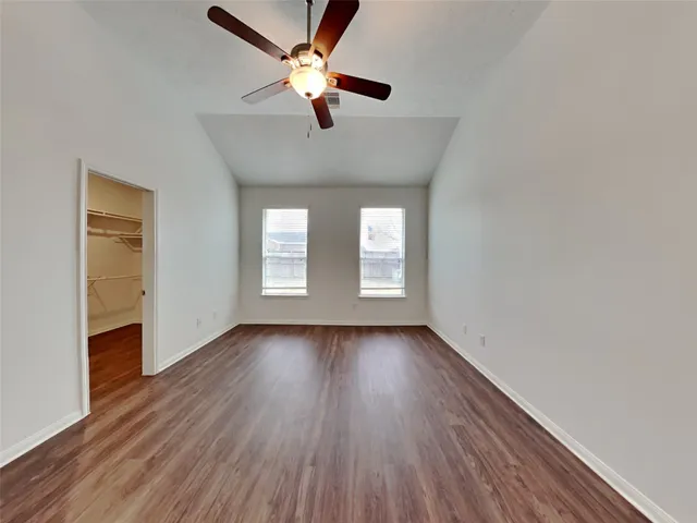 an empty room with wooden floor fan and windows