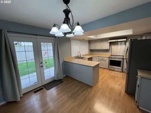 a large kitchen with stainless steel appliances granite countertop a refrigerator a sink dishwasher a stove and a dining table with wooden floor