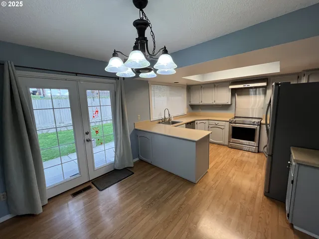 a large kitchen with stainless steel appliances granite countertop a refrigerator a sink dishwasher a stove and a dining table with wooden floor