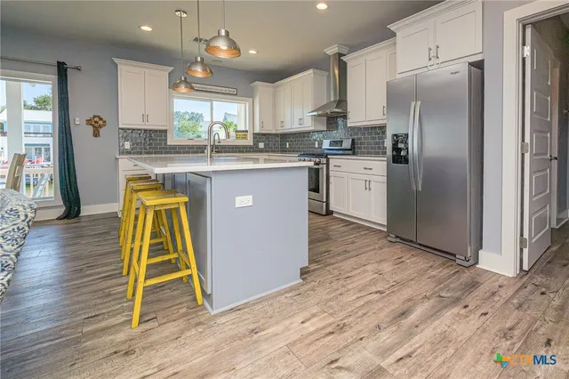 a kitchen with kitchen island granite countertop wooden floors stainless steel appliances a sink and a window